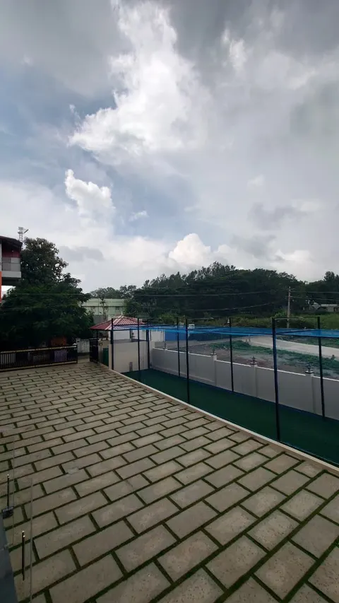 Floodlit cricket pitch with netting and a paved courtyard